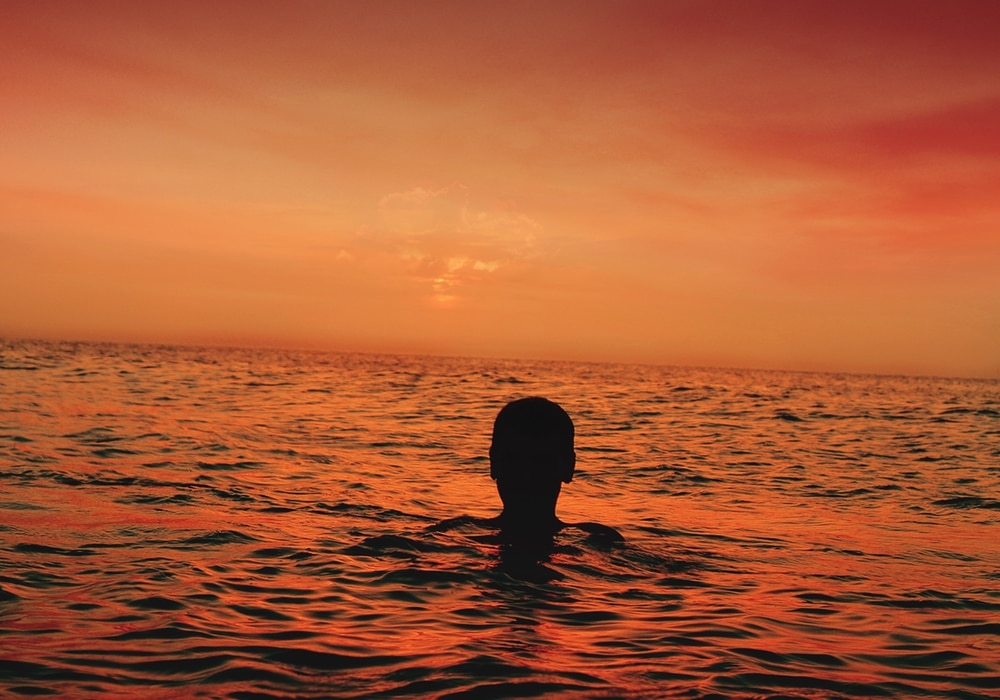 man swimming in the ocean during a sunset